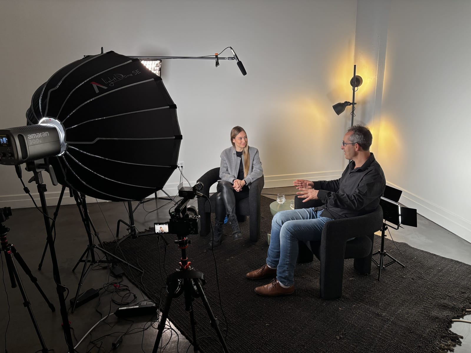 Nathan Jeffay and Camila Russo of The Defiant during a studio recording session - both seated in chairs facing each other, full lighting and camera rig visible.